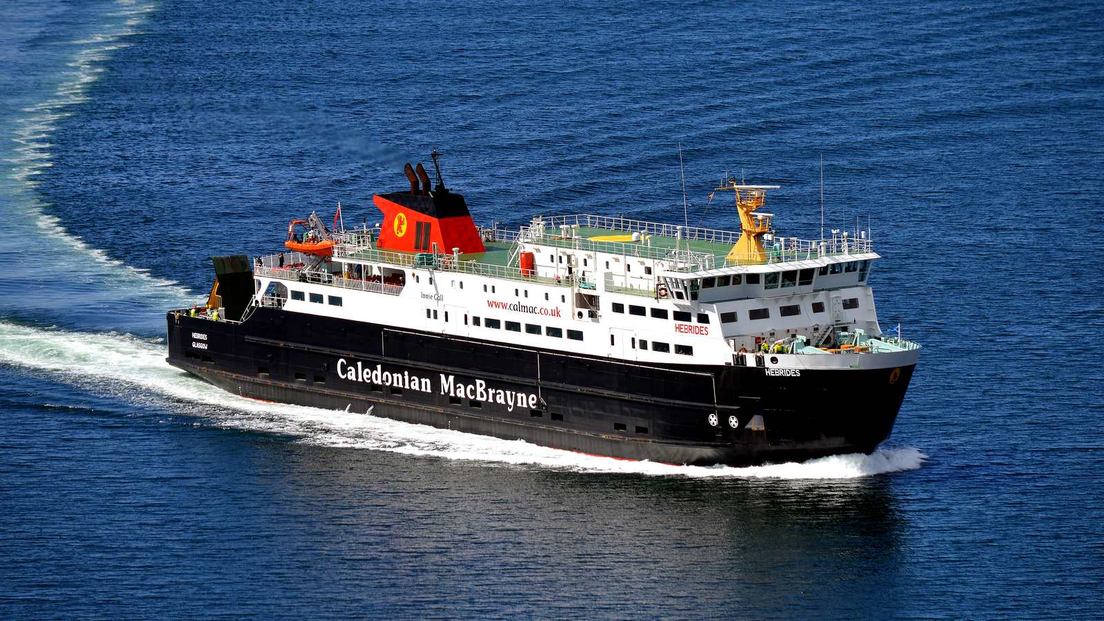 CalMac ferry MV Hebrides at speed on deep blue water, seen from above, with a long white wake behind it