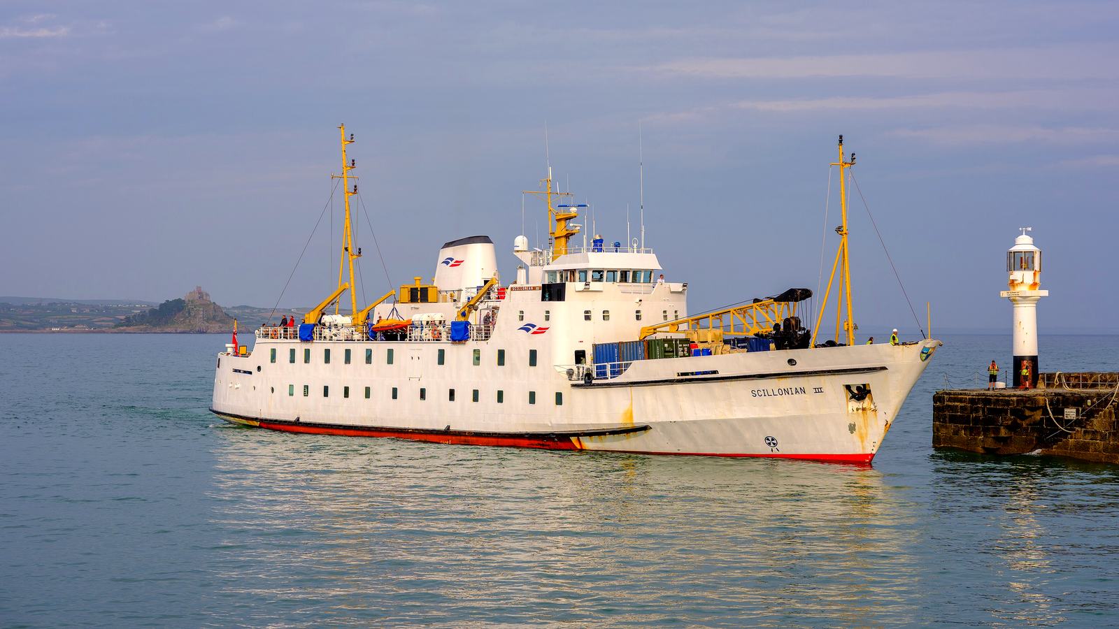 The white Scillonian III passenger ferry entering Penzance harbour past the lighthouse, with St Michael's Mount in the distance